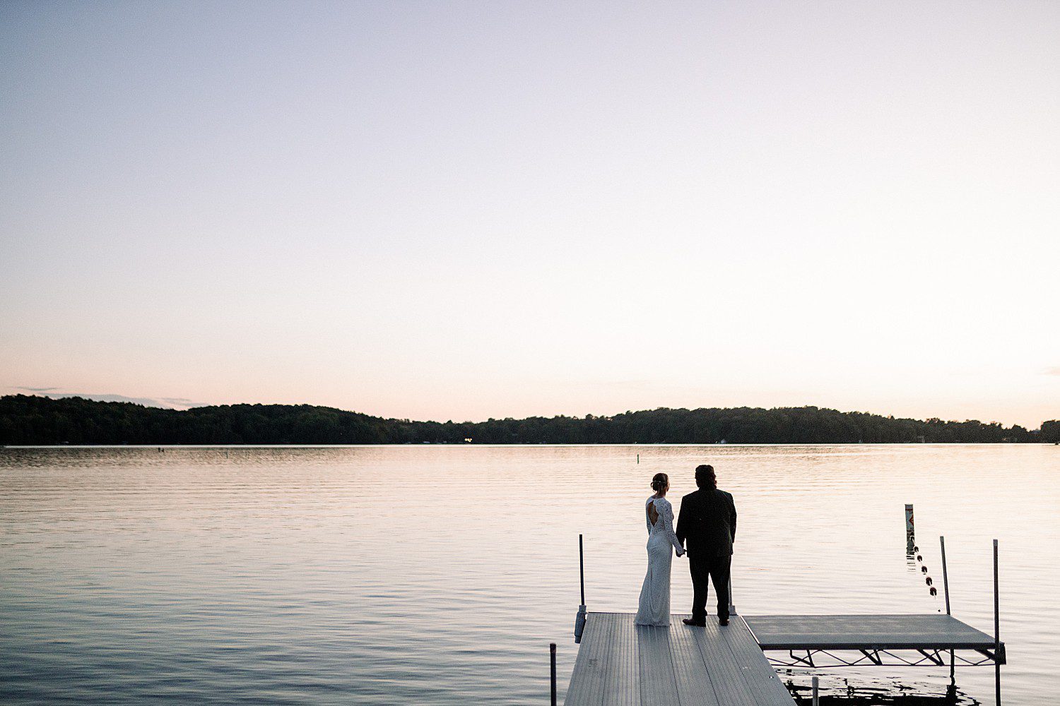 Kathryn and Logan standing on the dock looking out over Elkhart Lake at dusk at The Osthoff Resort in Elkhart Lake, Wisconsin