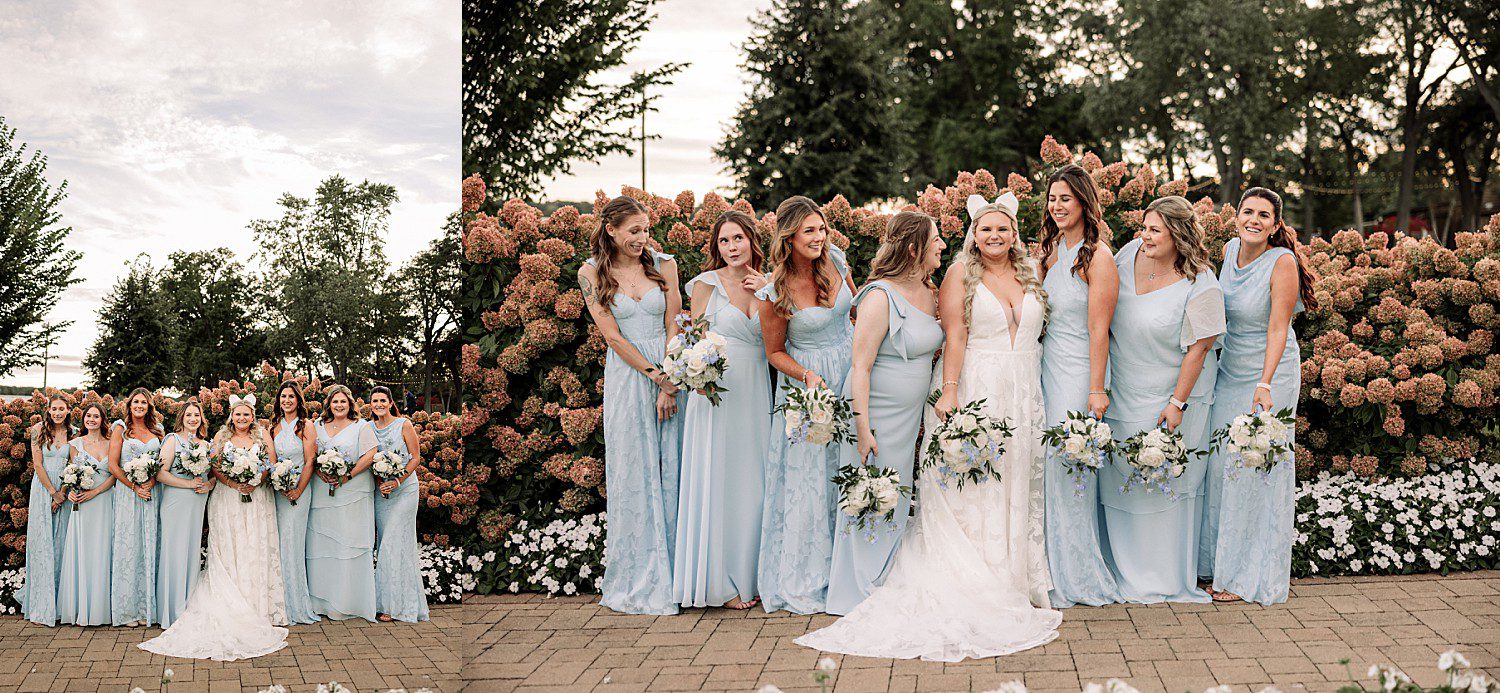 lakeside Wisconsin wedding in Delavan, Wisconsin: bride and bridesmaids holding bouquets in pale blue dresses beside flowering shrubs.