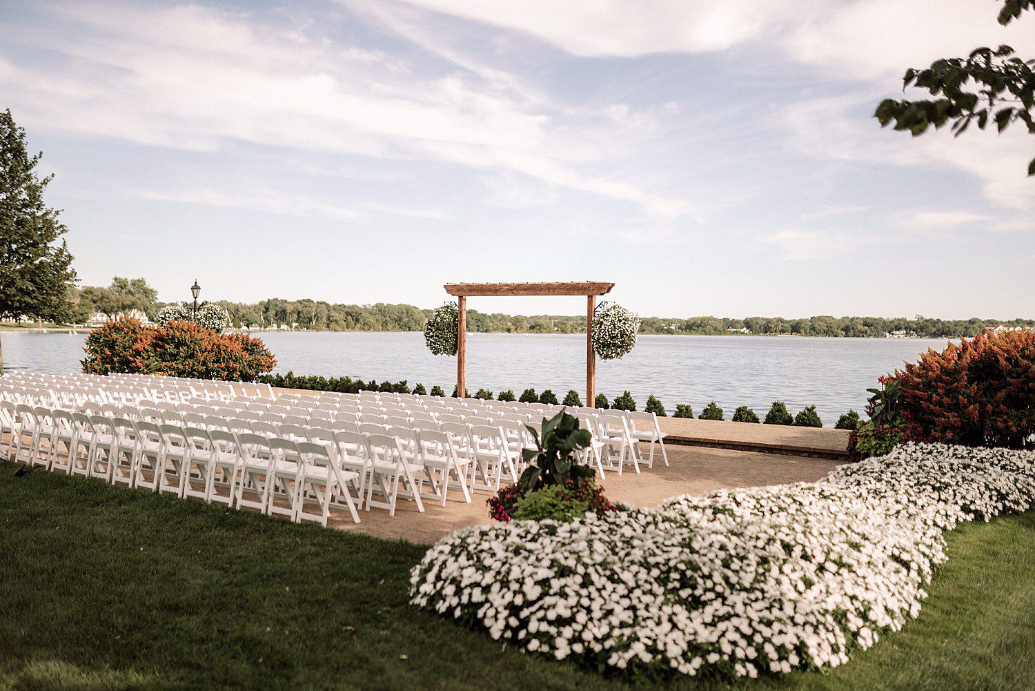 lakeside Wisconsin wedding in Delavan, Wisconsin: white ceremony chairs and a wooden arbor overlooking Delavan Lake.