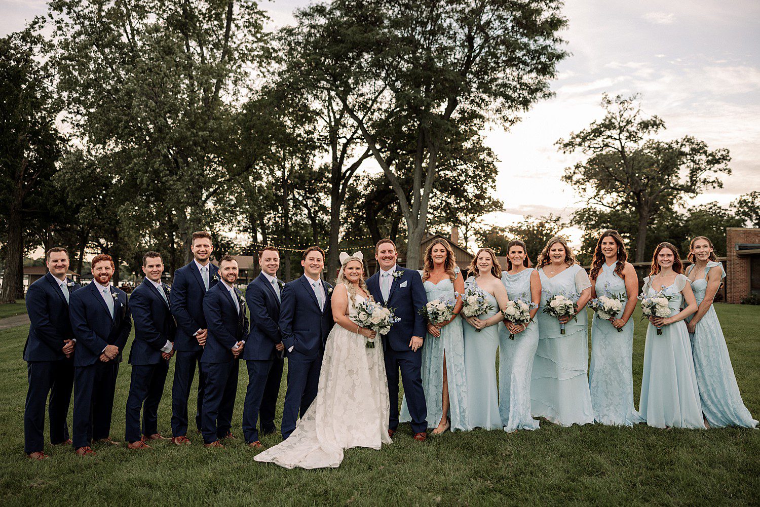 lakeside Wisconsin wedding in Delavan, Wisconsin: bride and groom with their wedding party beneath trees beside the lake.