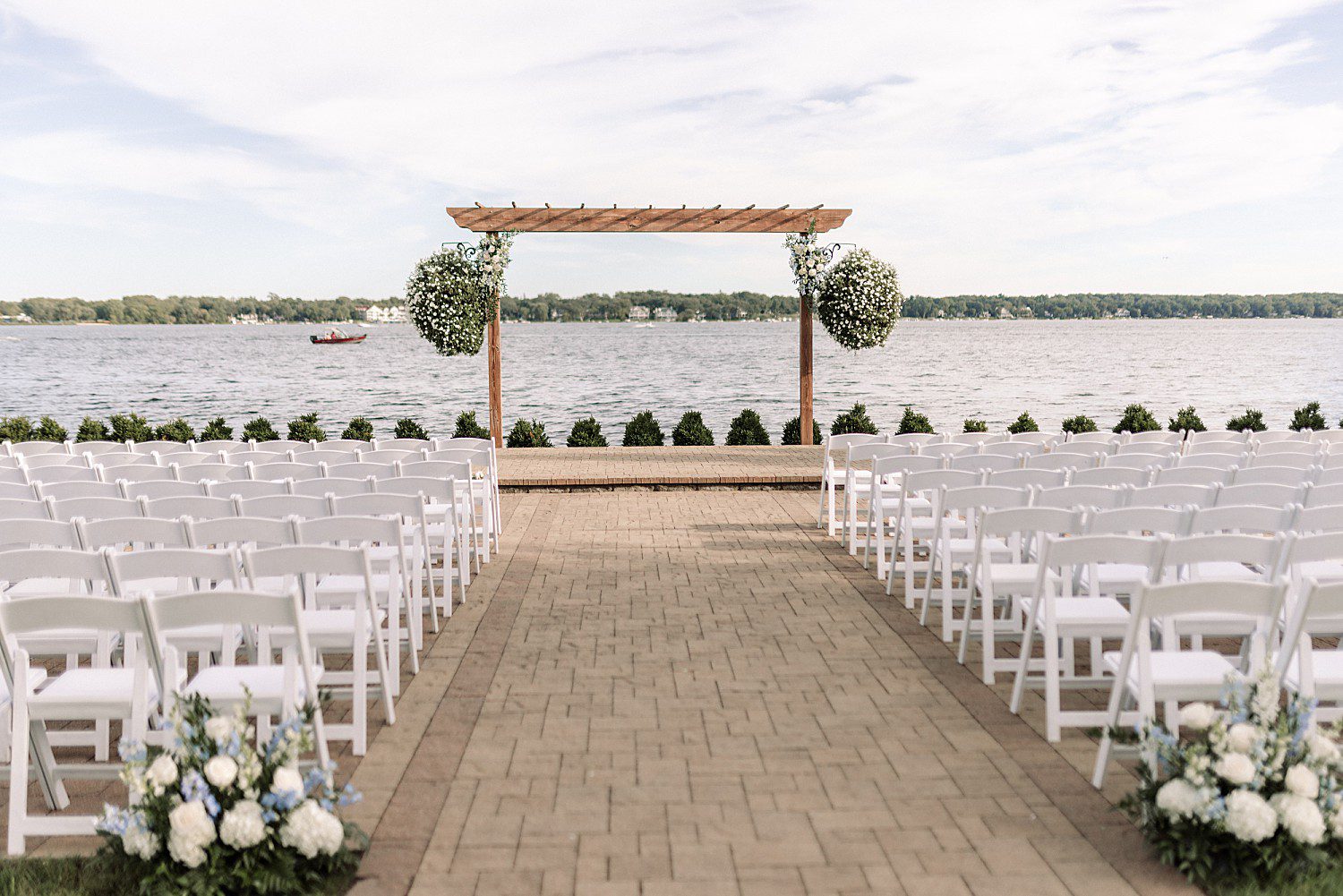 lakeside Wisconsin wedding in Delavan, Wisconsin: brick ceremony aisle lined with white chairs leading to a wooden lakeside arbor.