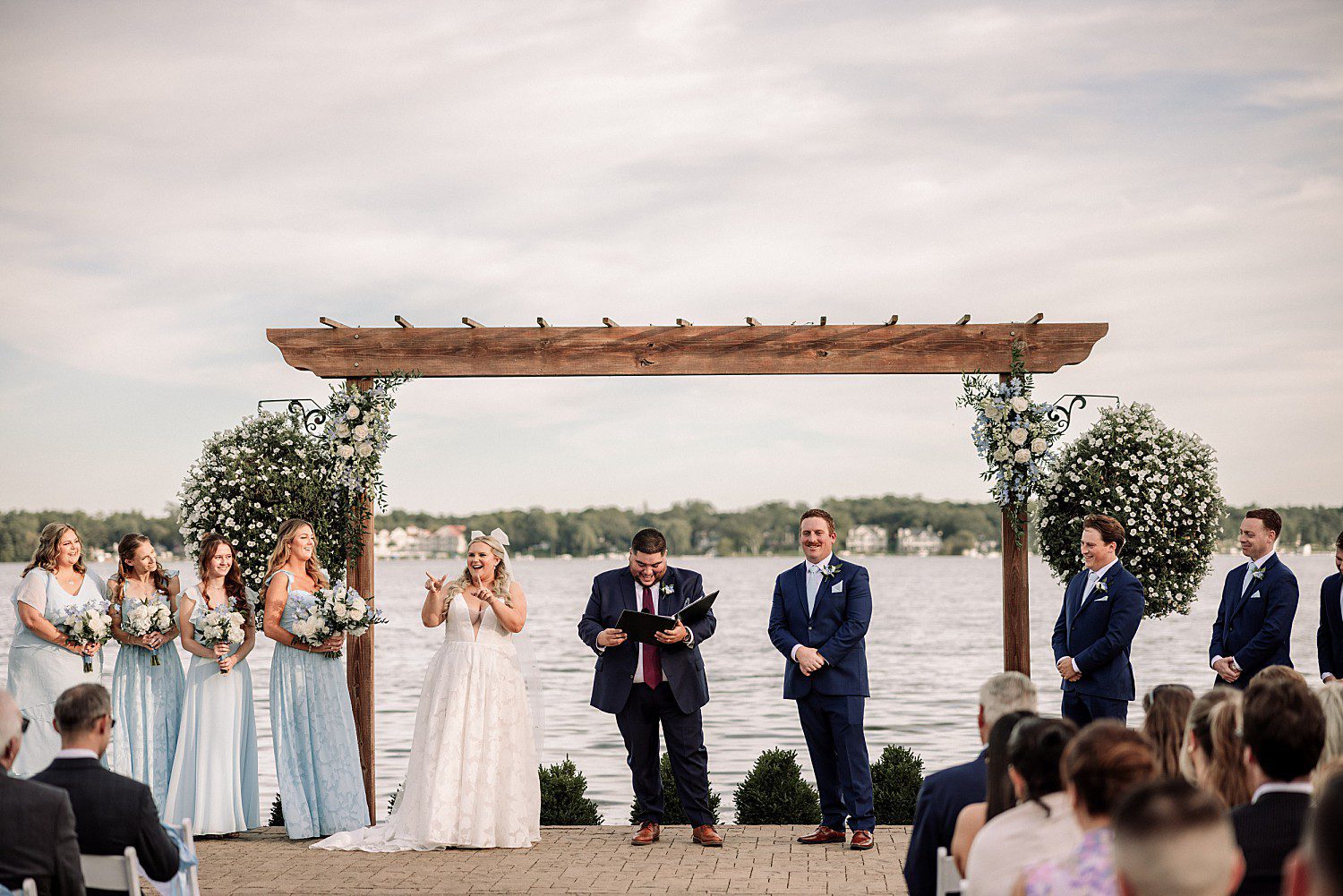 lakeside Wisconsin wedding in Delavan, Wisconsin: bride and groom standing with their officiant and wedding party beneath the lakeside arbor.